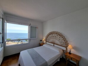 A bedroom with a bed, a window with a view of the sea, a decorative headboard, and bedside lamps. - Comfortable apartment with terrace 200m from the beach (L'Escala)