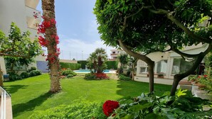 A well-maintained garden with a swimming pool, lush greenery, and flowering plants. - Comfortable apartment with terrace 200m from the beach (L'Escala)