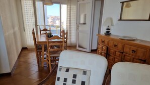 A hotel room with a dining area, a wooden cabinet, and a view of the city through the window. - Comfortable apartment with terrace 200m from the beach (L'Escala)
