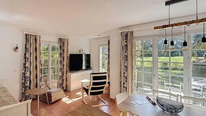 Ein Zimmer mit einem Bett, einem Fernseher, einem Esstisch, Stühlen, einem kleinen Tisch und Vorhängen.