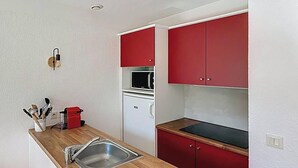 Eine kleine Küche mit Holzarbeitsplatte, Spüle, roten Schränken, einer Mikrowelle und einem kleinen Kühlschrank.