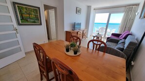 A dining area with a wooden table and chairs, a small plant on the table, and a view of the ocean through a large window. - Apartment in L'Escala with terrace and pool, near the beach (L'Escala)
