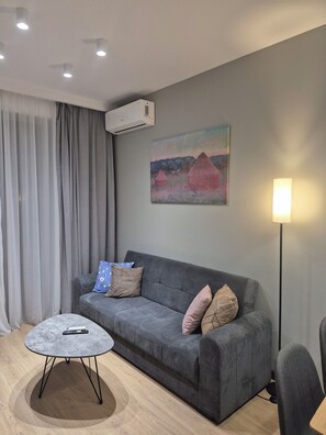 Ein modernes Wohnzimmer mit grauem Sofa, einem runden Couchtisch und einem Gemälde an der Wand.