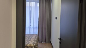 Una habitación de hotel con una cama, piso de madera y una puerta que da a otra estancia.