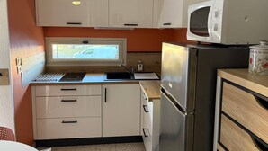 A compact kitchen with white cabinets, a stainless steel refrigerator, a microwave, and a window with a view of a parked car. - Air-conditioned studio near the thermal baths (Balaruc-les-Bains)