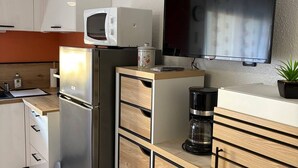 A compact kitchen with a refrigerator, microwave, coffee maker, and a flat-screen TV mounted on the wall. - Air-conditioned studio near the thermal baths (Balaruc-les-Bains)