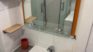 A bathroom with a glass shelf, a red bucket, a white sink, and a glass shower enclosure. - Air-conditioned studio near the thermal baths (Balaruc-les-Bains)