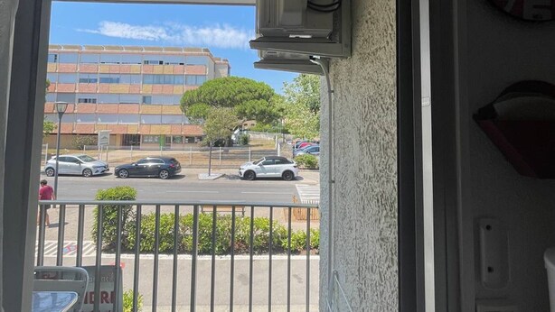A view from a balcony with a building, cars, and a tree in the background. - Air-conditioned studio near the thermal baths (Balaruc-les-Bains)
