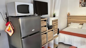 A compact hotel room with a bed, a small desk with a TV, a refrigerator, and a kitchenette area. - Air-conditioned studio near the thermal baths (Balaruc-les-Bains)