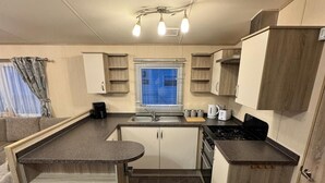 A compact kitchen with a central island, a stove, and a sink. - 3 Bedroom, Lyons Oakfield, Towyn, Pets Welcome (Rhyl)