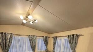 A compact living space with a sofa, a television, and curtains on the windows. - 3 Bedroom, Lyons Oakfield, Towyn, Pets Welcome (Rhyl)