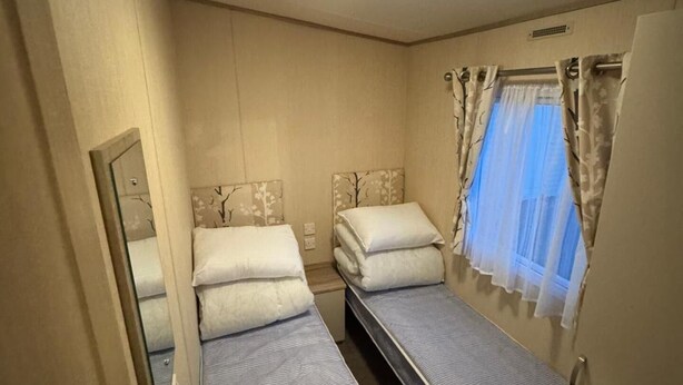 A compact room with two single beds, a mirror, a window with curtains, and a ceiling light. - 3 Bedroom, Lyons Oakfield, Towyn, Pets Welcome (Rhyl)