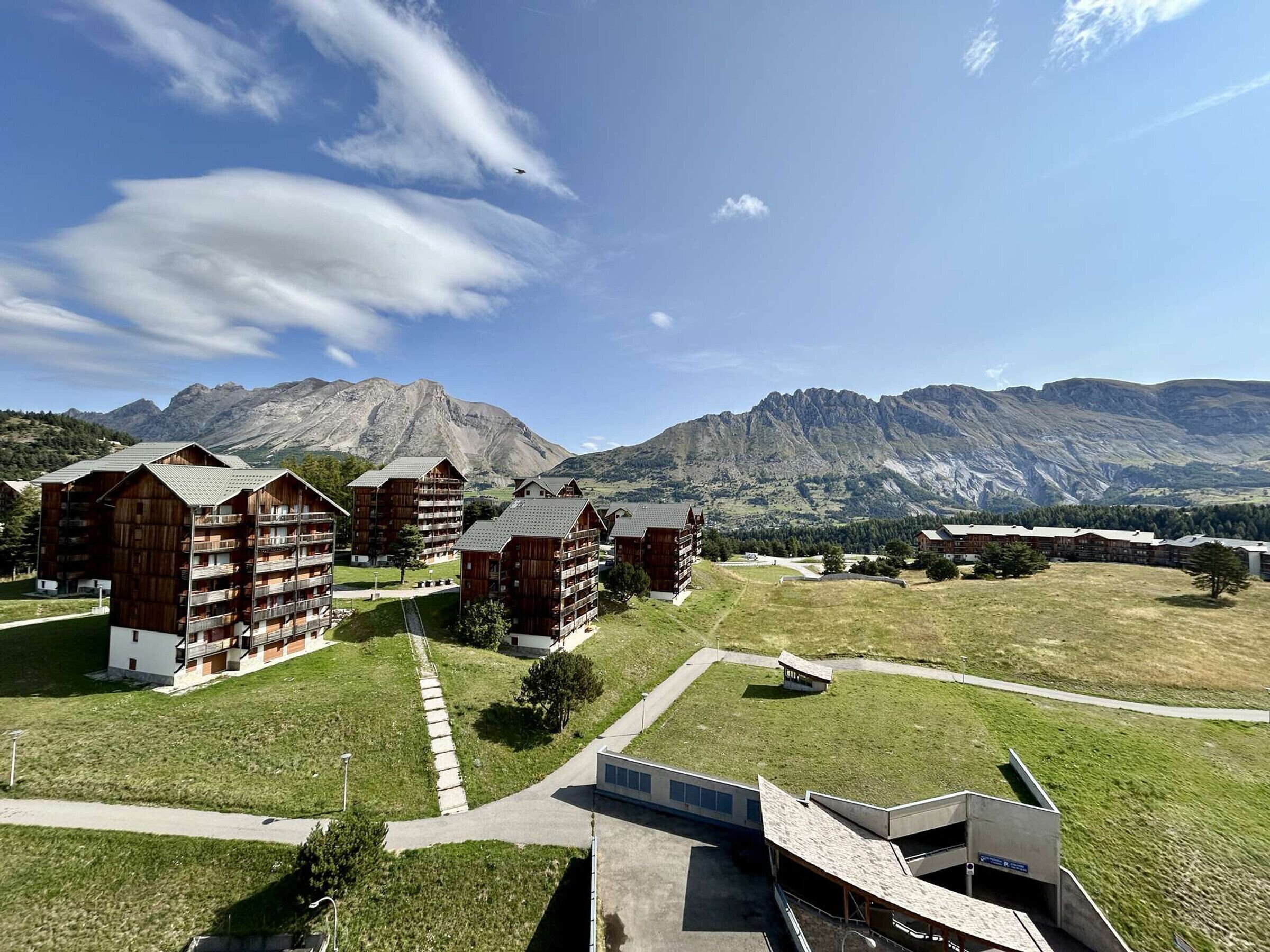 Un chalet composé de plusieurs bâtiments en bois, un espace de stationnement et un paysage montagneux en arrière-plan.