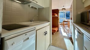 Une cuisine compacte avec des meubles blancs, un lave-vaisselle encastré et une fenêtre donnant sur un coin repas.