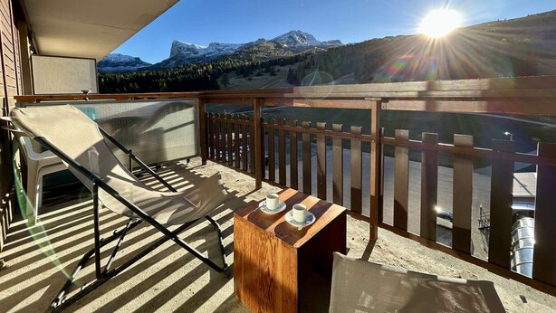 Un balcon avec un transat, une petite table avec des tasses et une vue sur des montagnes enneigées.