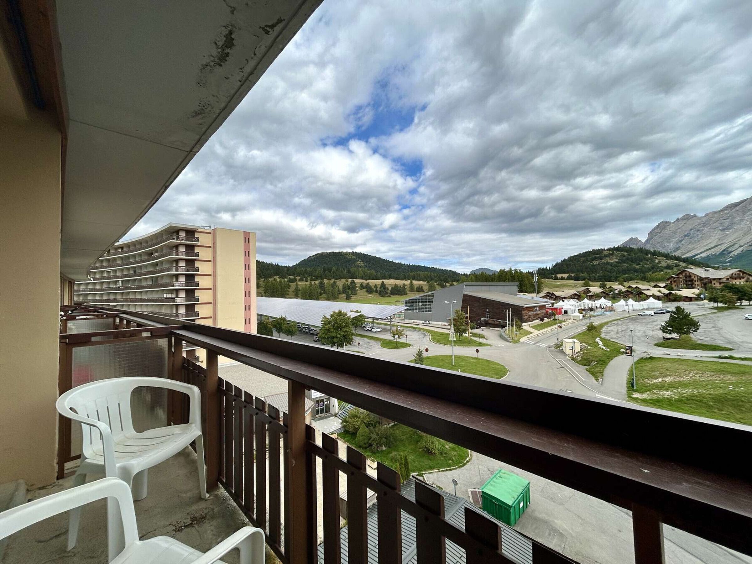 Un balcon offrant une vue sur un immeuble d’hôtel, un parking et des montagnes en arrière-plan.