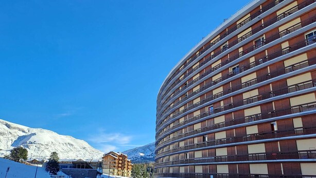 Un hôtel à plusieurs étages, doté de balcons, qui se dresse sur un fond de montagnes enneigées.