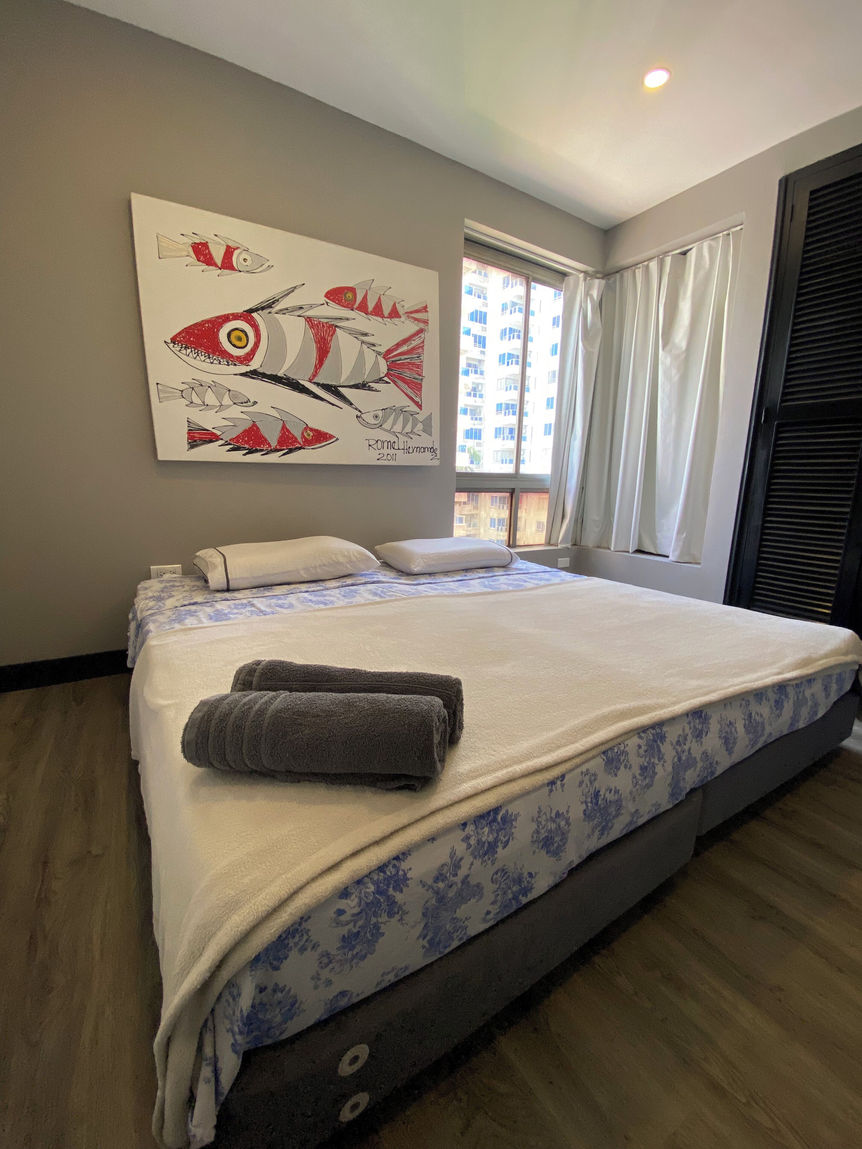 A hotel room with a large bed, a painting on the wall, and a window with curtains.