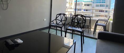 A modern room with a glass table, chairs, a sofa, and a TV mounted on the wall.