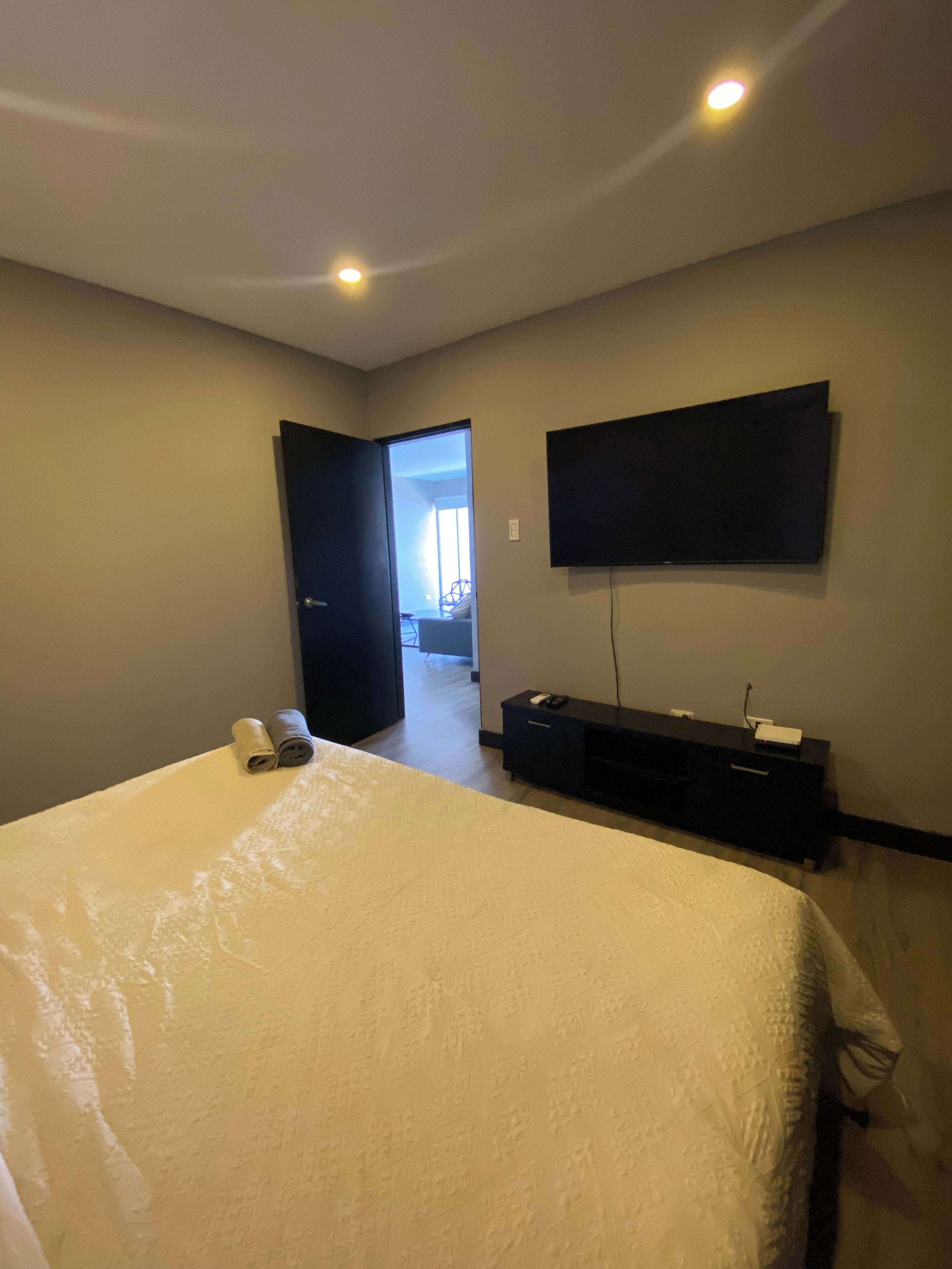 Quarto com cama grande, televisão de tela plana na parede e porta que dá para outro cômodo.