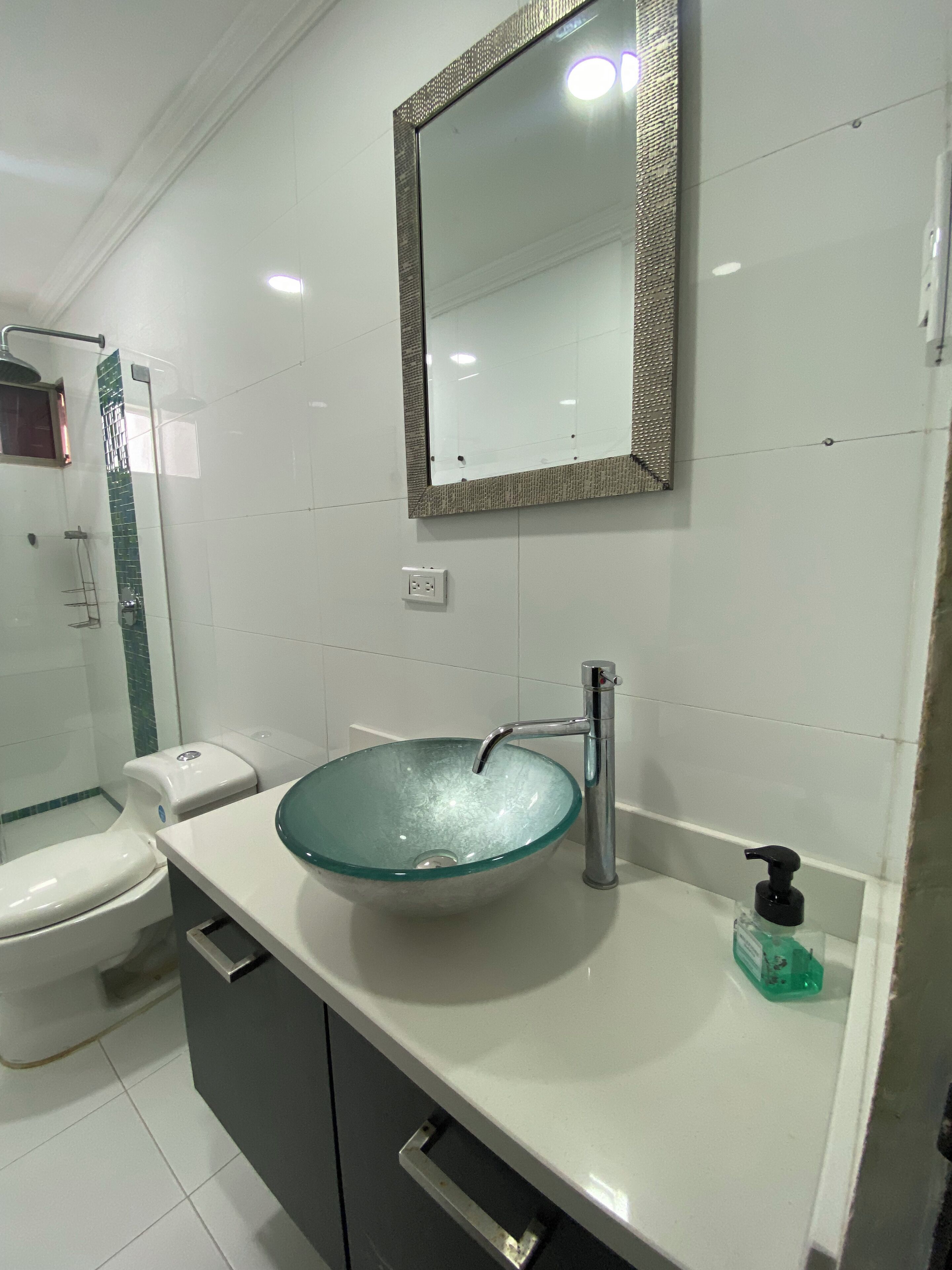 Ein Badezimmer mit einem Glaswaschbecken, einem modernen Spiegel und einer Toilette.