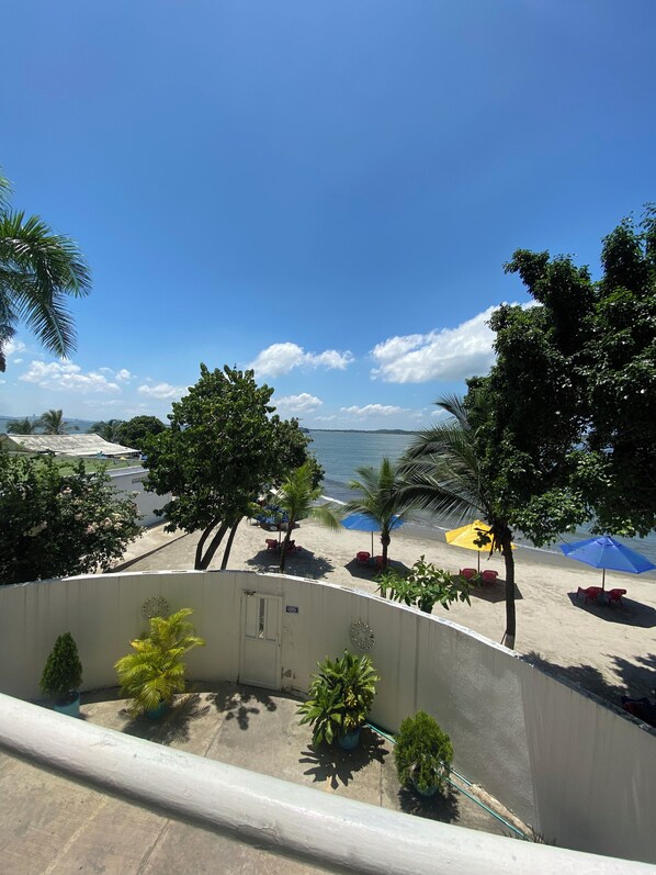 Un balcón con vista a una playa, palmeras y un cielo azul despejado.