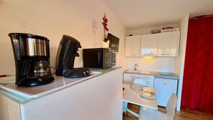 Une cuisine compacte équipée d’une machine à café, d’un four à micro-ondes et d’une petite table à manger avec des chaises.