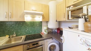 A compact kitchen with wooden cabinets, a microwave, a washing machine, and a green-tiled backsplash. - Studio cabin 4 people at slope base in Gourette (Gourette)