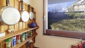 A kitchen with wooden shelves holding pots, pans, and jars of condiments. A window reveals a view of a building and a grassy area. - Studio cabin 4 people at slope base in Gourette (Gourette)