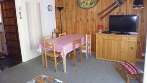 A cozy room with a wooden wall, a dining table with chairs, a television, and a small cabinet. - Studio cabin 4 people at slope base in Gourette (Gourette)