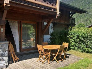 Eine Holzdielen-Terrasse mit Tisch und Stühlen, eine Glastür und ein Berg im Hintergrund.