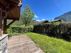 Eine Holzterrasse, ein Heckenstreifen und eine Bergkulisse.