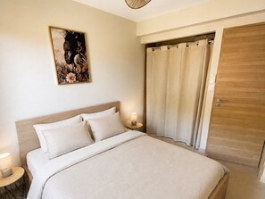 A bedroom with a bed, a nightstand, a wall-mounted painting, a curtain, and a wooden door. - Lovely T2 Cabin - Near Beach & Shops (Bormes-les-Mimosas)
