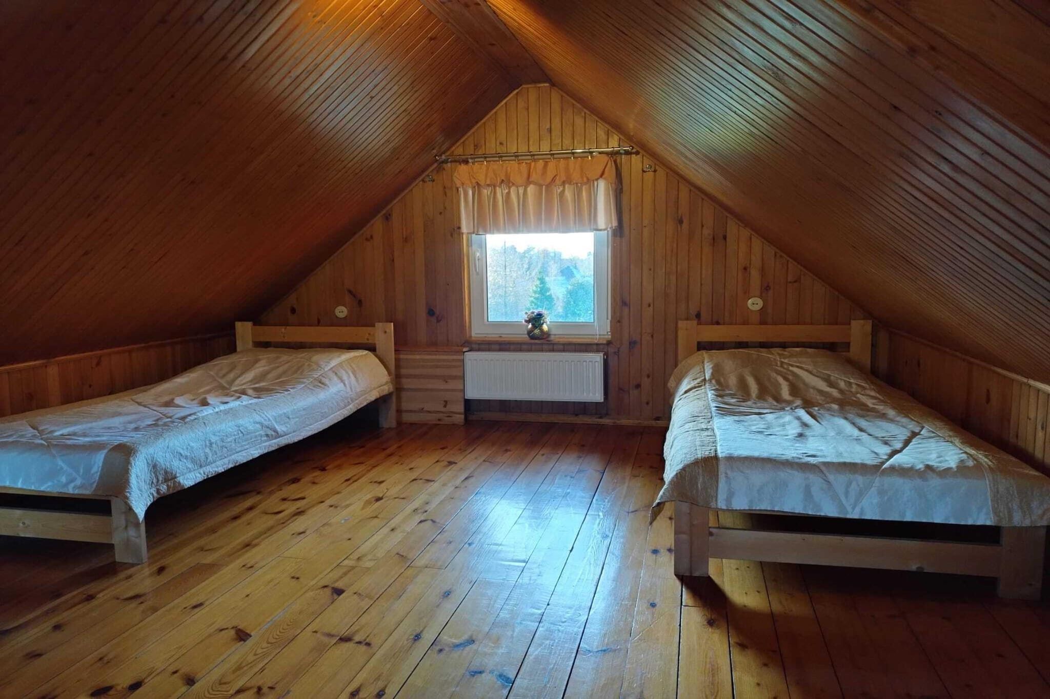 Ein kleines Schlafzimmer im Dachgeschoss mit zwei hölzernen Betten, einem Fenster mit Blick auf Bäume und einer Heizung unter dem Fenster.