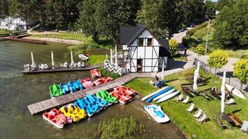 A lakeside property with a dock, colorful inflatable boats, a building with a sloped roof, and a grassy area with seating.