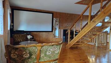 A wooden interior with a staircase, a large screen, and a floral-patterned sofa.