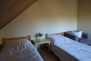 A room with two beds, a small table with a vase, and a sofa.