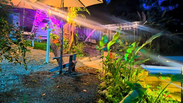 Un jardín exterior con una sombrilla grande, plantas en macetas y un espacio de estar.