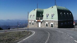 Un bâtiment en pierre doté d’un toit végétalisé et de nombreuses fenêtres, situé à un carrefour et offrant une vue dégagée sur le paysage environnant.