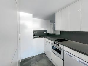 Una cocina moderna con armarios blancos, encimera negra y electrodomésticos de acero inoxidable.