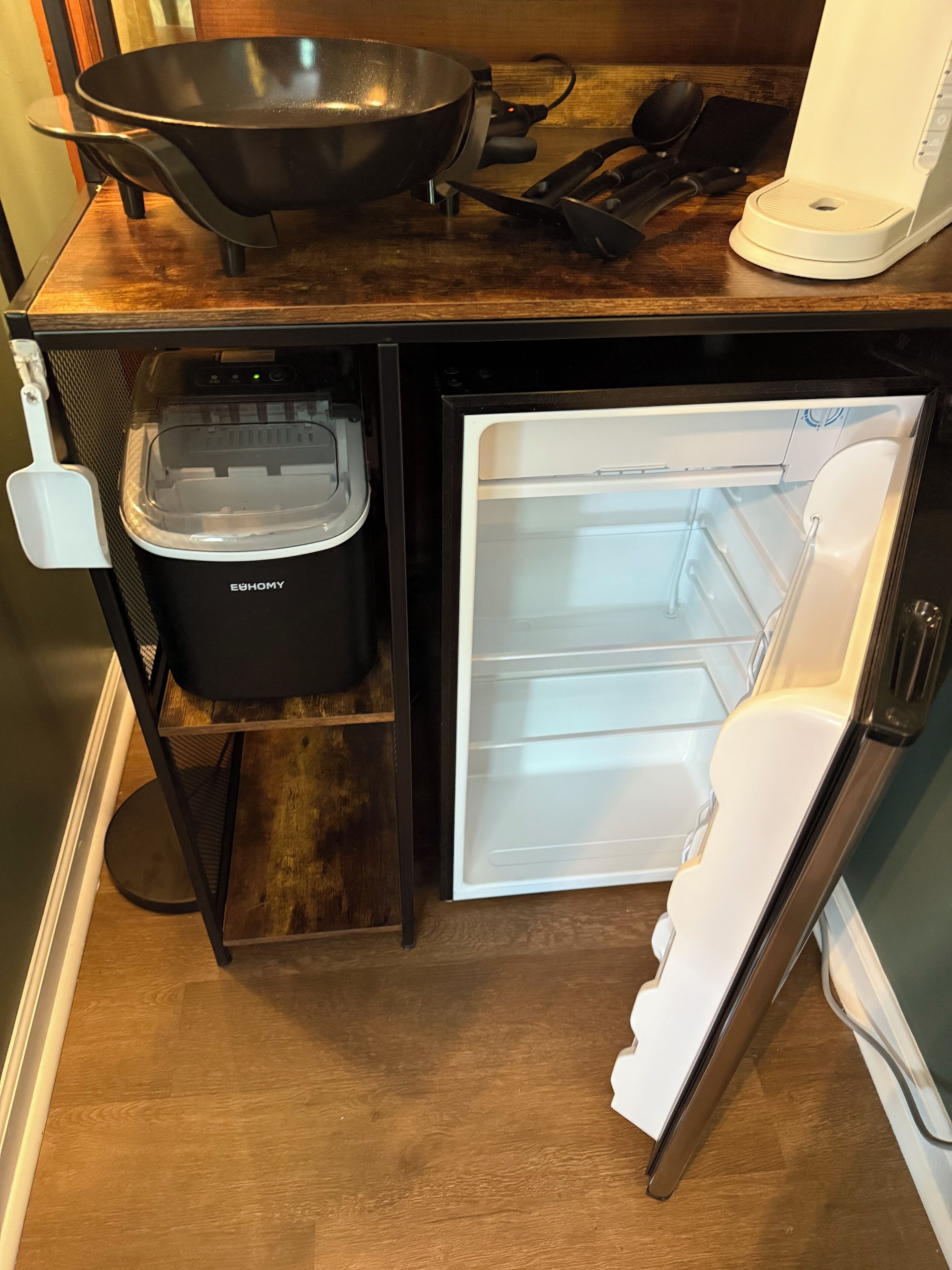 Eine kompakte Küche mit einem eingebauten Kühlschrank, einem schwarzen Mixer und einem Wok auf der Arbeitsfläche.