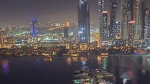 Un port de plaisance avec des bateaux amarrés, une vue sur les gratte-ciel d’une ville, dont les bâtiments sont illuminés, et un pont en arrière-plan.