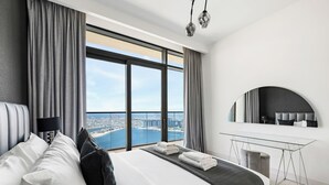 Une chambre d’hôtel moderne, dotée d’un grand lit, d’un bureau et offrant une vue sur le paysage urbain.