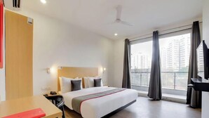 A hotel room with a bed, a desk, a chair, a TV, and a window with curtains. - FLORA RESIDENCY (Gurugram)