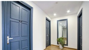 A hallway with wooden flooring, blue doors, and a potted plant. - FLORA RESIDENCY (Gurugram)