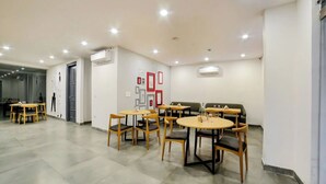 A spacious room with multiple round tables and chairs, air conditioning units, and framed pictures on the walls. - FLORA RESIDENCY (Gurugram)