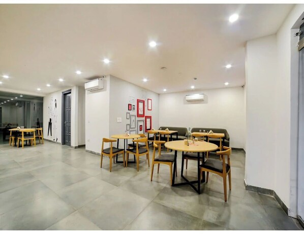 A spacious room with multiple round tables and chairs, air conditioning units, and framed pictures on the walls. - FLORA RESIDENCY (Gurugram)