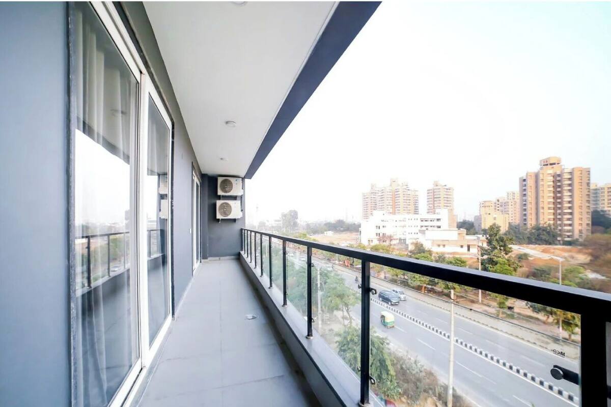 A balcony with large windows, air conditioning units, and a view of a cityscape with buildings and a road.