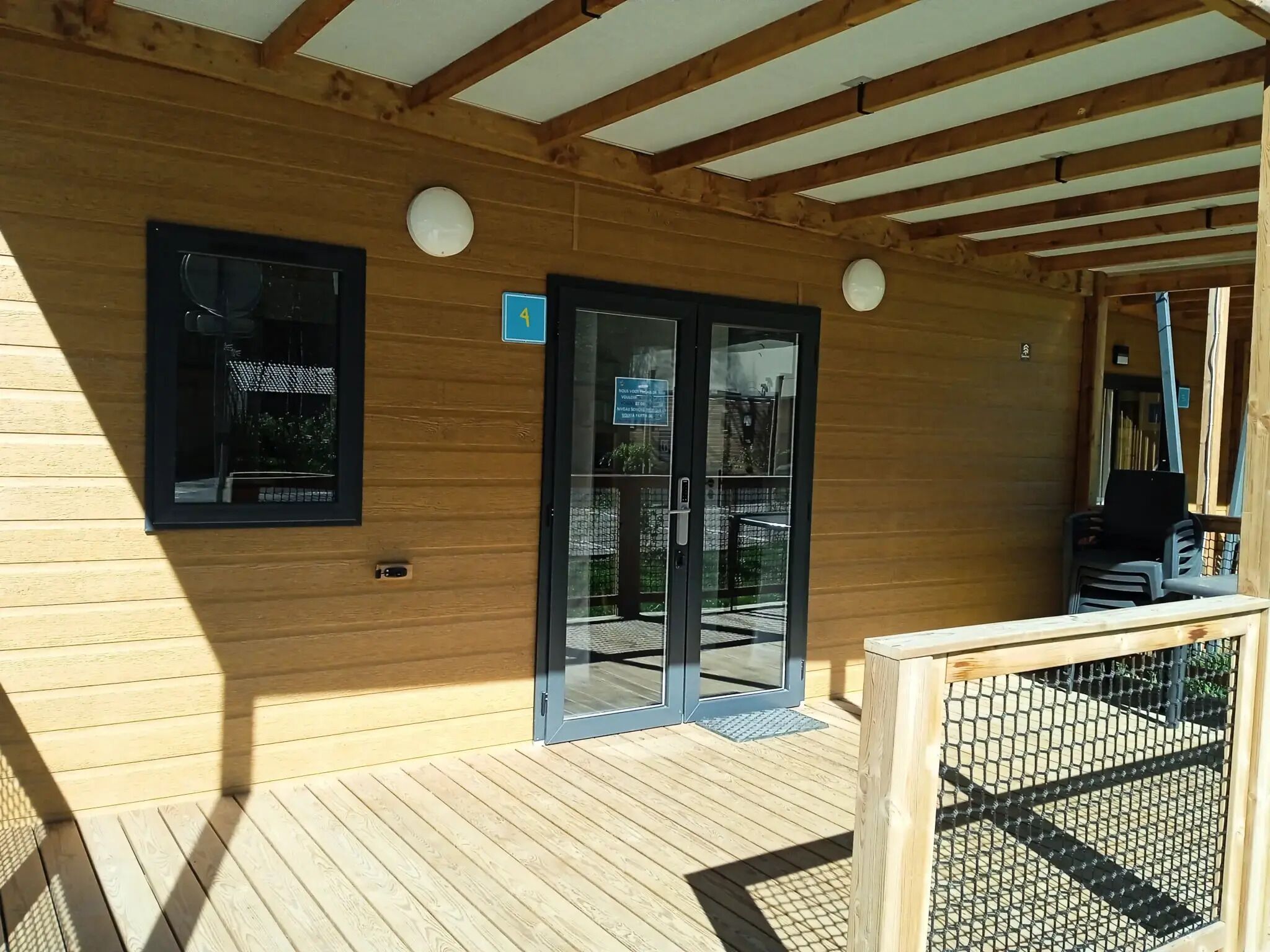 A wooden exterior with a glass door entrance, a small sign above the door, and a wooden deck with a railing.