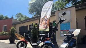 Una patineta estacionada frente a un edificio con un cartel anunciando 'The Coolest Rides'.